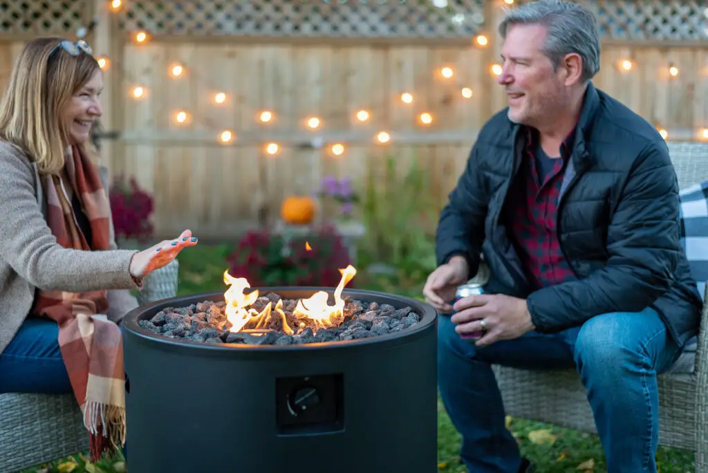 Happy couple relaxing around a propane fire pit in their backyard with string lights
